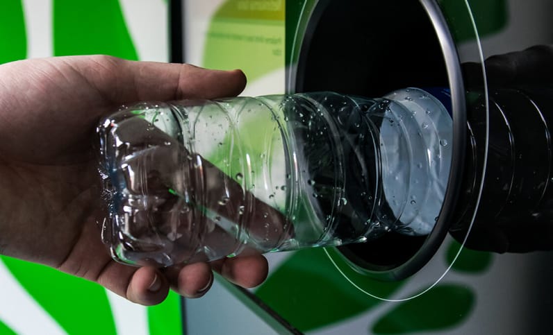 Мужская рука кладет пластиковую бутылку в отверстие автомата, который принимает пластик в качестве оплаты вместо денег.